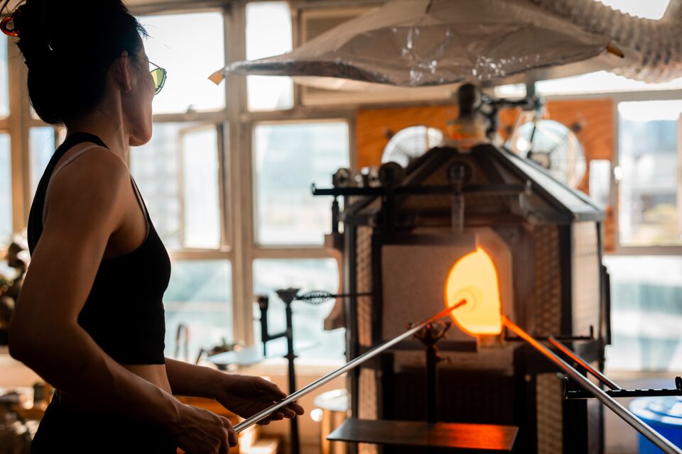 A glassmaker shaping hot glass in front of the studio furnace